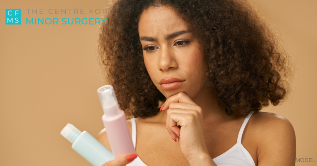 Attractive young woman with curly hair looking doubtful while choosing between two cream products (model)